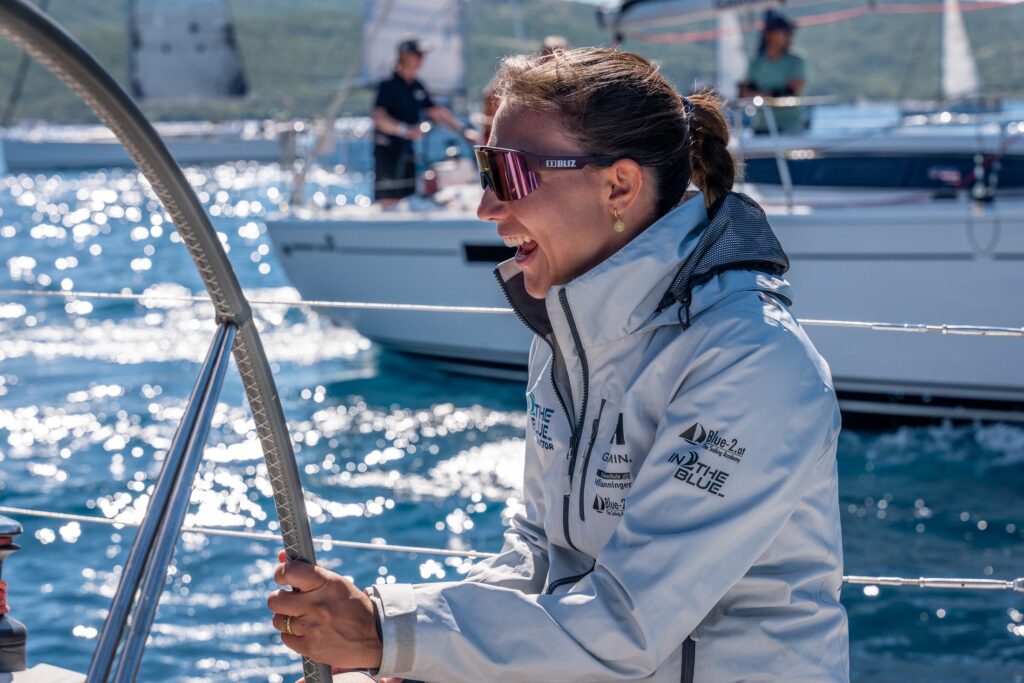 Sailor in IN2THEBLUE jacket smiling at the helm of a yacht